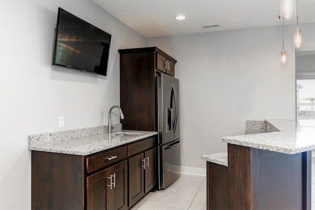 kitchen featuring visible vents, stainless steel refrigerator with ice dispenser, a sink, dark brown cabinetry, and a peninsula