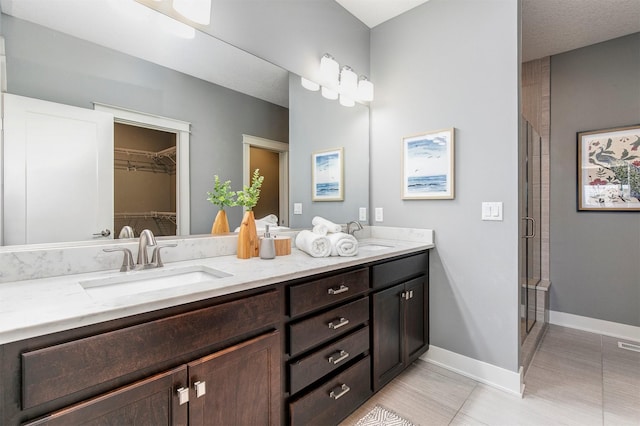 bathroom with a shower stall, a walk in closet, baseboards, double vanity, and a sink