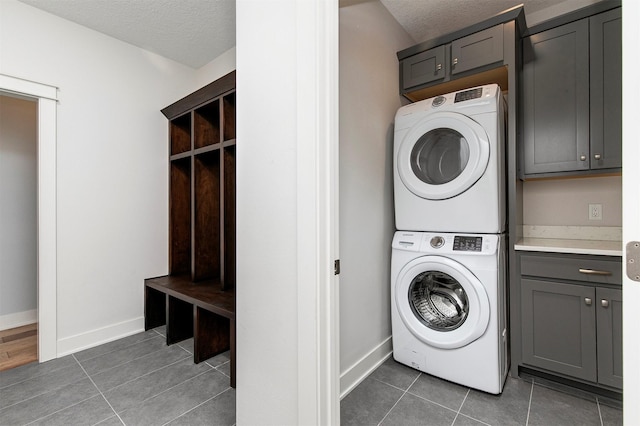 washroom with tile patterned flooring, cabinet space, a textured ceiling, and stacked washing maching and dryer