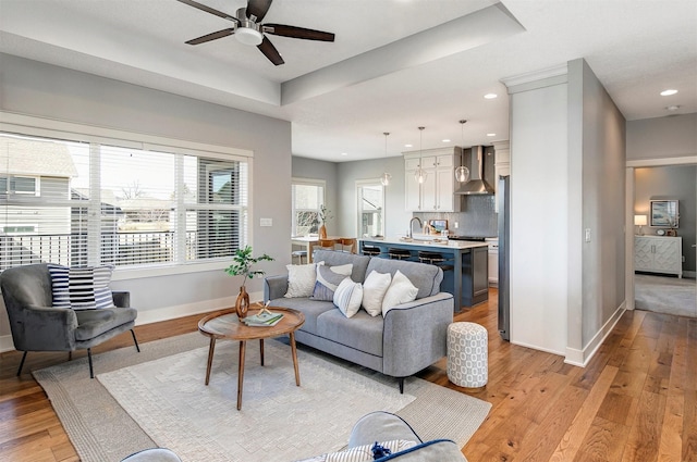 living room featuring ceiling fan, baseboards, a tray ceiling, and light wood-style floors