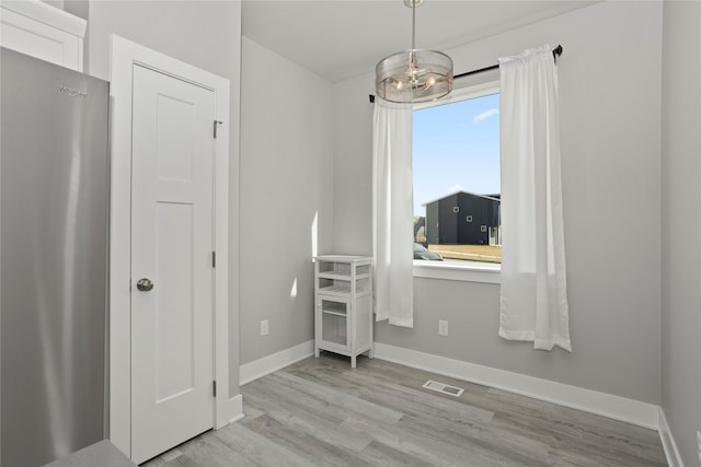 interior space featuring visible vents, baseboards, a chandelier, freestanding refrigerator, and wood finished floors