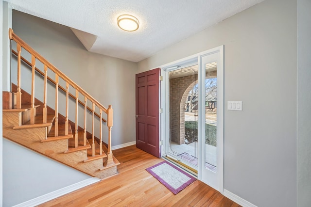 foyer with stairs, wood finished floors, baseboards, and a textured ceiling