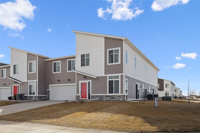 view of front of home with stone siding, an attached garage, concrete driveway, and central AC