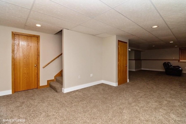 finished basement featuring a paneled ceiling, stairway, carpet floors, and baseboards