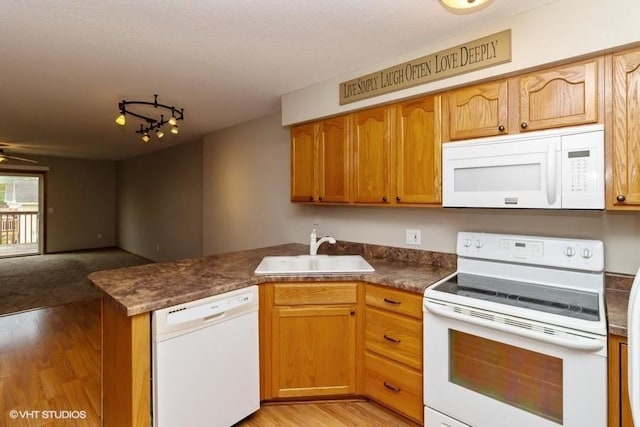 kitchen featuring white appliances, light wood-style flooring, a peninsula, and a sink