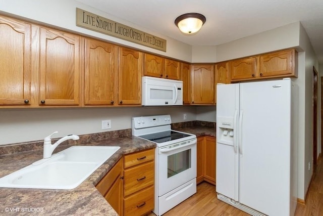 kitchen with a sink, dark countertops, white appliances, light wood-style floors, and brown cabinetry