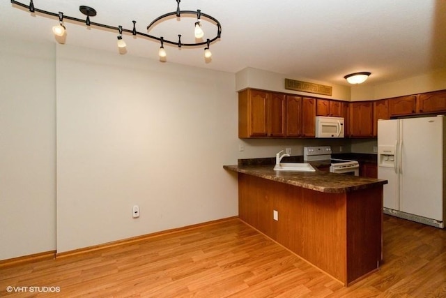 kitchen featuring dark countertops, a peninsula, light wood-style floors, white appliances, and a sink