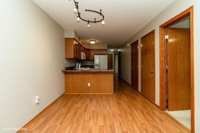 kitchen with brown cabinets, light wood-style flooring, a sink, white appliances, and a peninsula