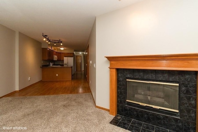 unfurnished living room with track lighting, carpet flooring, baseboards, and a tile fireplace