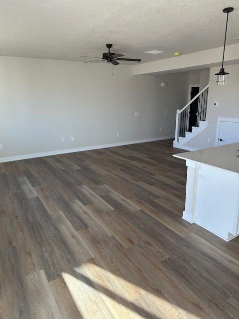 unfurnished living room with dark wood-type flooring, stairway, baseboards, and ceiling fan