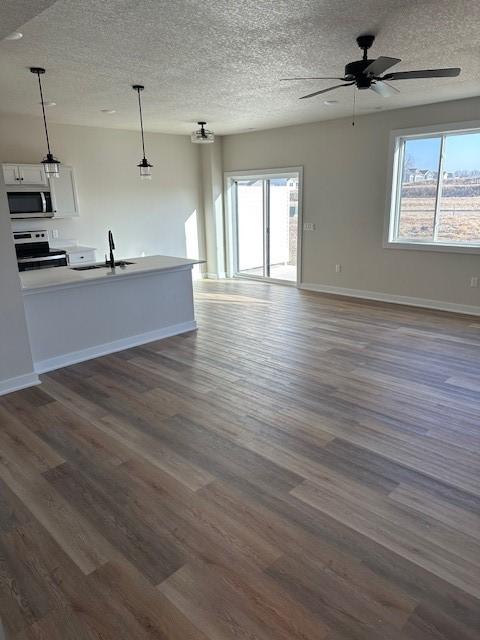 unfurnished living room featuring a sink, baseboards, dark wood-type flooring, and ceiling fan
