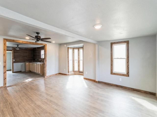 unfurnished living room featuring ceiling fan, baseboards, light wood-style floors, a textured ceiling, and a sink