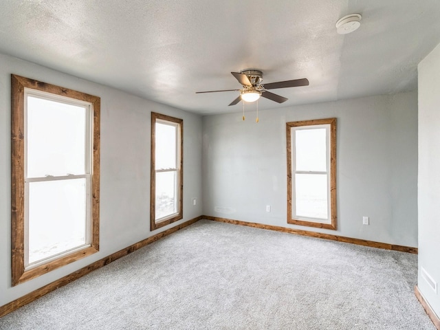 carpeted empty room with a ceiling fan, baseboards, and a textured ceiling