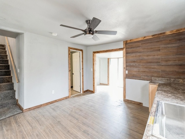 unfurnished room with light wood-type flooring, a sink, wood walls, baseboards, and stairs