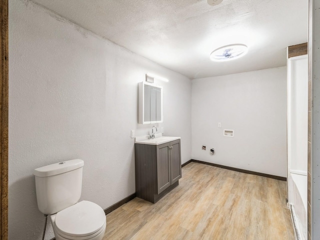 half bath with baseboards, toilet, vanity, wood finished floors, and a textured ceiling