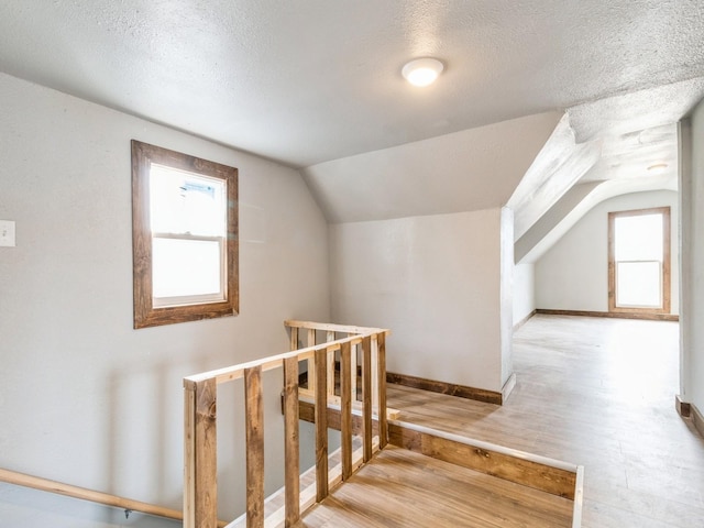 additional living space with baseboards, a textured ceiling, wood finished floors, and vaulted ceiling