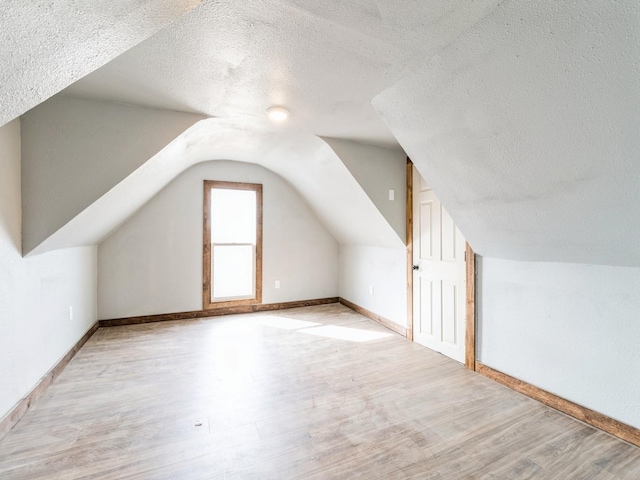 additional living space with vaulted ceiling, baseboards, light wood-type flooring, and a textured ceiling