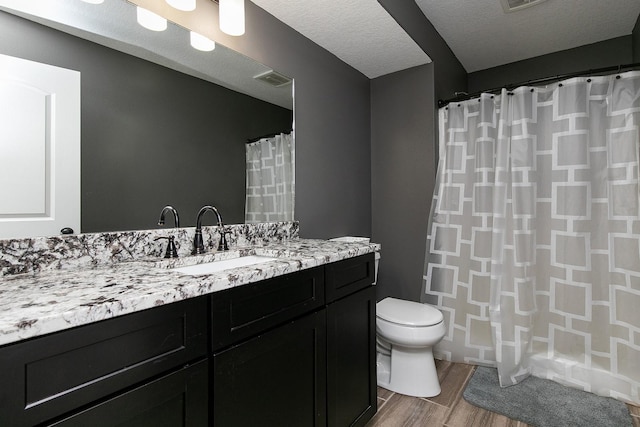 bathroom featuring visible vents, toilet, vanity, wood finished floors, and a textured ceiling