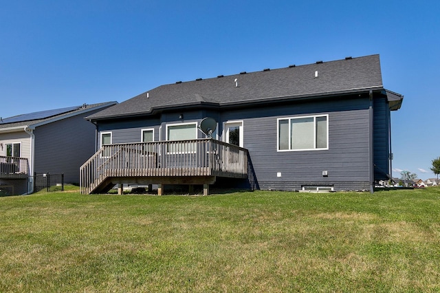 rear view of property with a deck, a lawn, and roof with shingles