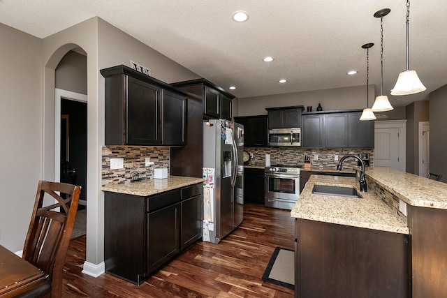 kitchen with a sink, light stone countertops, appliances with stainless steel finishes, and dark wood finished floors