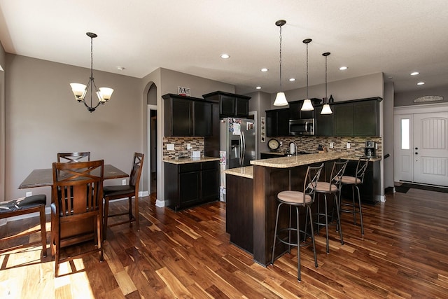 kitchen featuring a kitchen bar, dark wood-type flooring, arched walkways, and stainless steel appliances