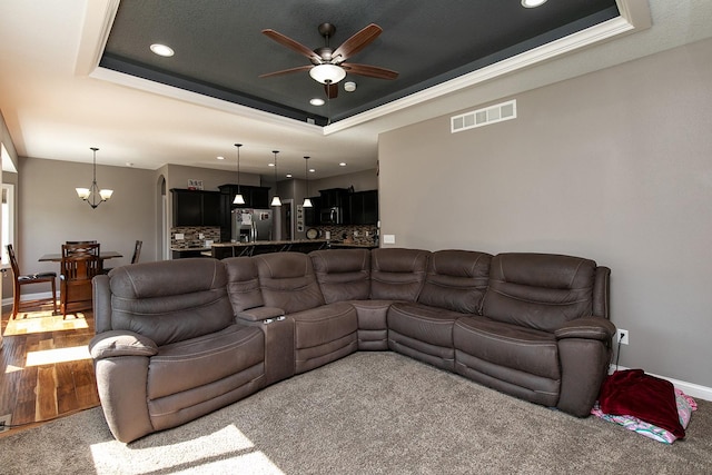 living area with visible vents, a raised ceiling, baseboards, and ceiling fan with notable chandelier