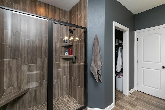 full bathroom with a spacious closet, baseboards, a stall shower, and wood finish floors