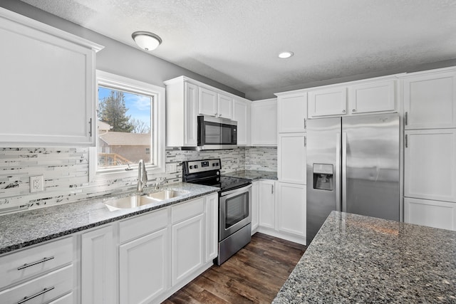 kitchen featuring dark stone countertops, appliances with stainless steel finishes, dark wood-style floors, white cabinetry, and a sink