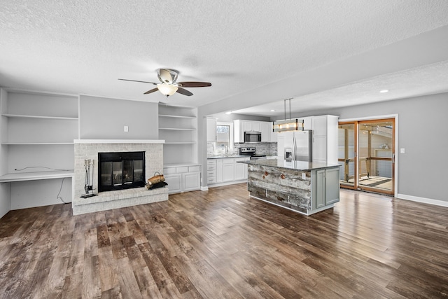 unfurnished living room with baseboards, dark wood finished floors, ceiling fan, a textured ceiling, and a brick fireplace