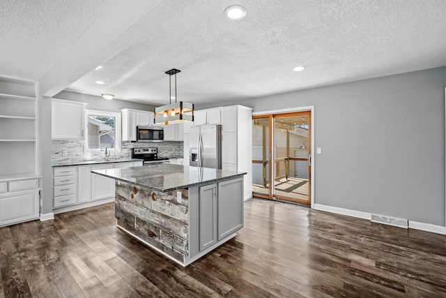 kitchen with a sink, backsplash, appliances with stainless steel finishes, and dark wood-style floors