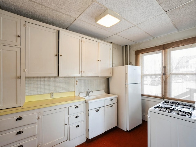 kitchen with a drop ceiling, light countertops, white cabinets, white appliances, and a sink