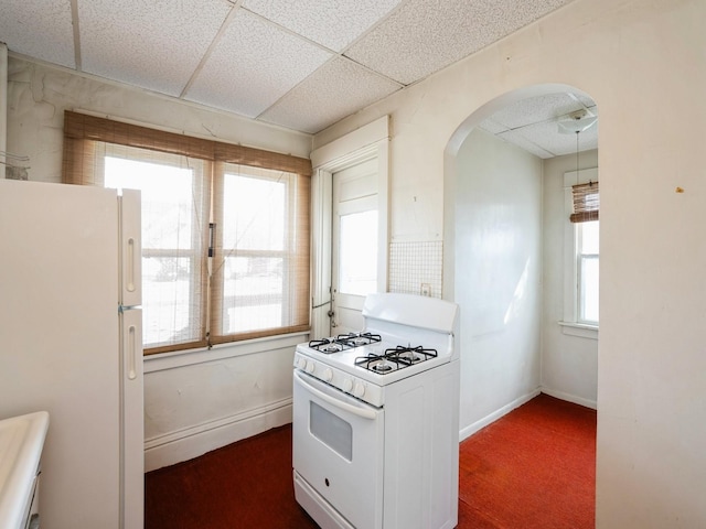 kitchen featuring arched walkways, white appliances, a paneled ceiling, and baseboards