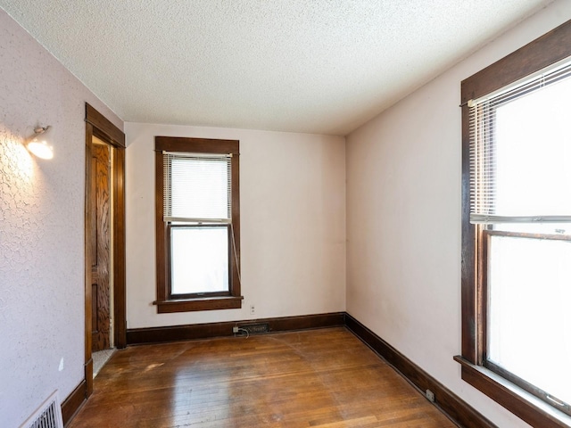 empty room with visible vents, a textured ceiling, wood-type flooring, baseboards, and a textured wall