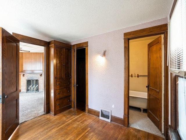 unfurnished bedroom with a brick fireplace, wood finished floors, visible vents, and a textured ceiling