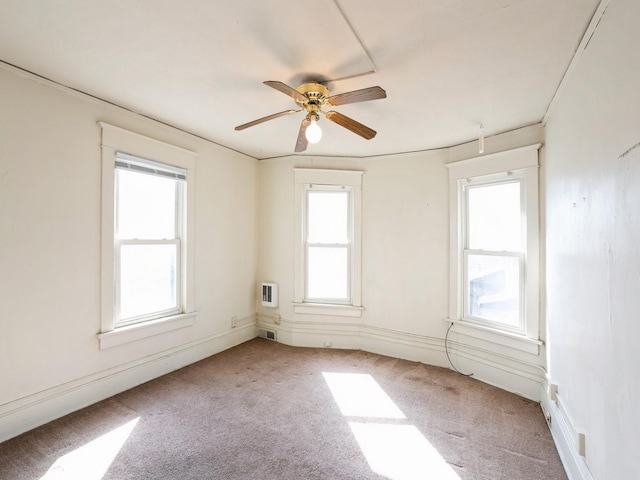 empty room with visible vents, heating unit, light colored carpet, and a ceiling fan