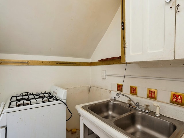 kitchen with white range with gas cooktop, lofted ceiling, a sink, light countertops, and white cabinets