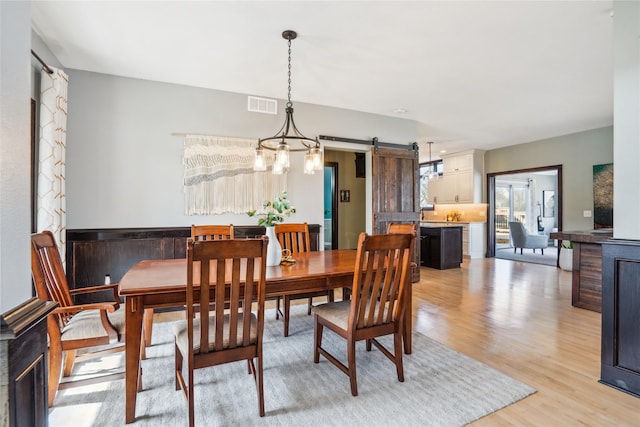 dining room featuring a barn door, visible vents, and light wood-type flooring