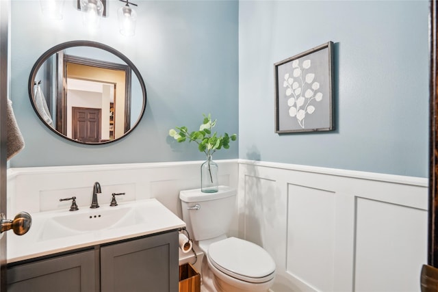 half bathroom with a wainscoted wall, toilet, and vanity