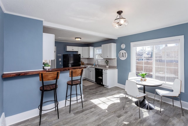 kitchen featuring a kitchen bar, black appliances, backsplash, white cabinetry, and light wood-style floors