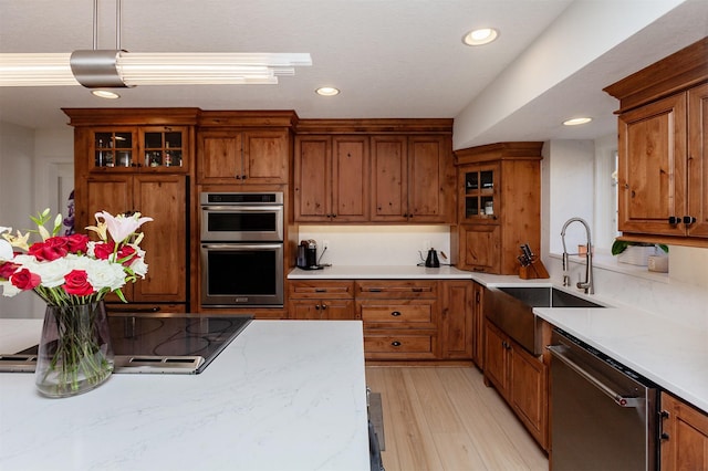 kitchen with glass insert cabinets, brown cabinets, appliances with stainless steel finishes, light wood-style flooring, and a sink