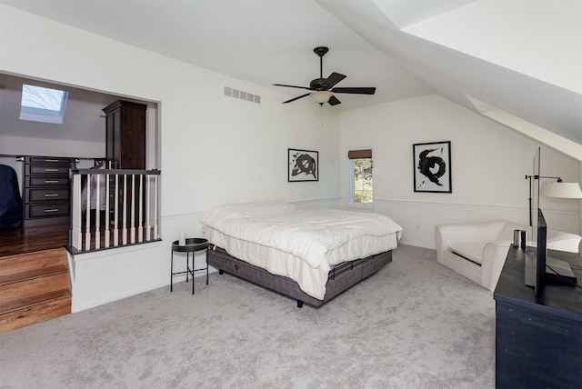 carpeted bedroom featuring visible vents, vaulted ceiling with skylight, baseboards, and ceiling fan