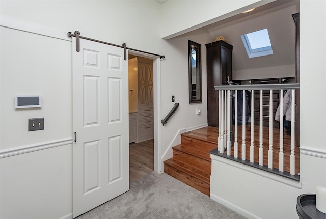 stairway featuring a barn door, wood finished floors, baseboards, and lofted ceiling with skylight