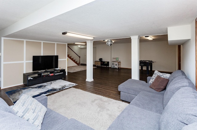 living area featuring a textured ceiling, wood finished floors, stairs, and decorative columns