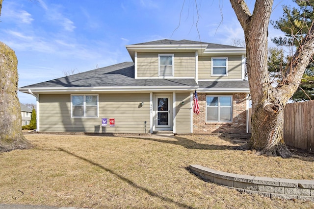 view of front of home with a front yard, fence, brick siding, and a shingled roof