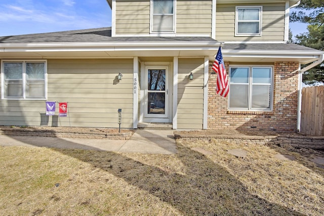 entrance to property with fence, brick siding, and roof with shingles