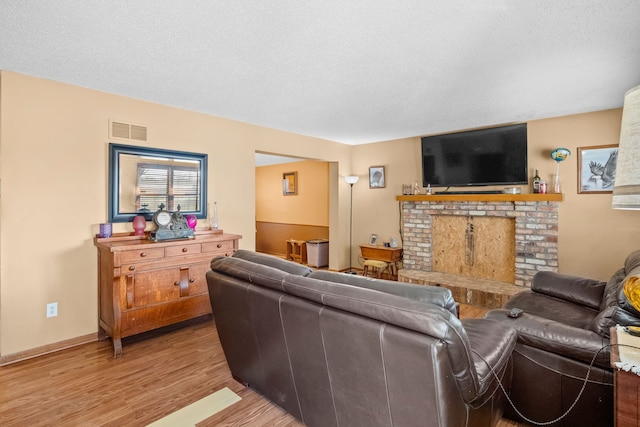 living room featuring a brick fireplace, light wood-type flooring, visible vents, baseboards, and a textured ceiling