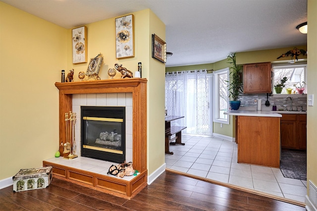 kitchen with tasteful backsplash, a tiled fireplace, light countertops, light wood-style floors, and a sink