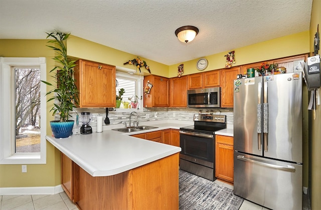 kitchen with light countertops, brown cabinets, a peninsula, stainless steel appliances, and a sink