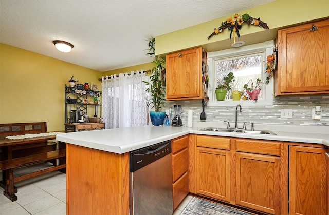 kitchen featuring backsplash, light countertops, a peninsula, stainless steel dishwasher, and a sink