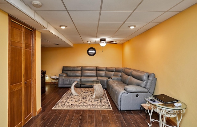 living room featuring ceiling fan, a drop ceiling, and dark wood finished floors